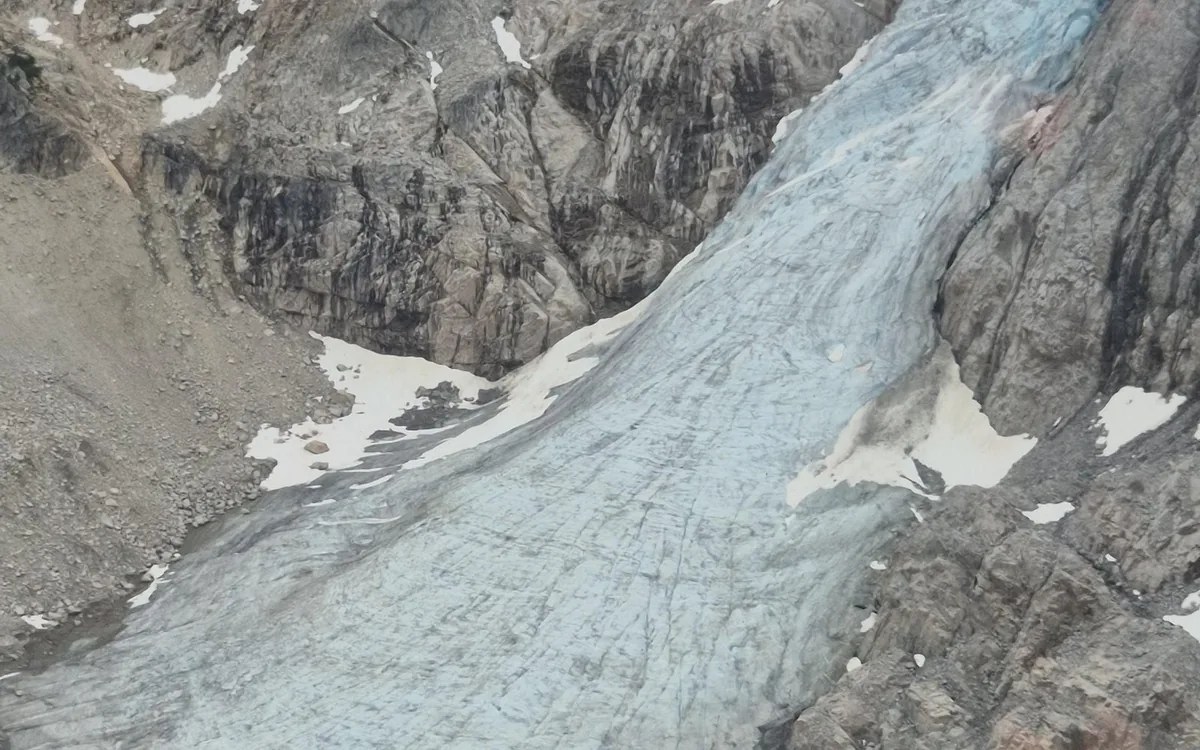 A pale blue glacier tongue running down a gully between dark broken rock