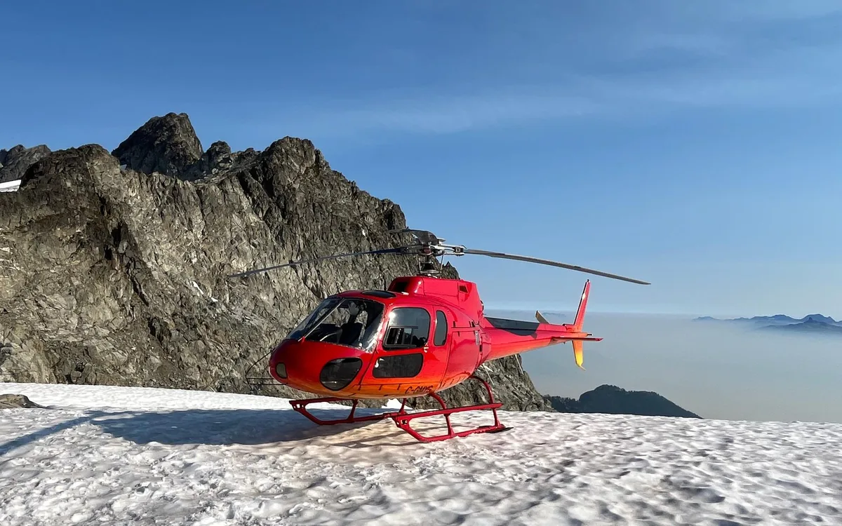 A red helicopter standing on a snowfield in the mountains after landing