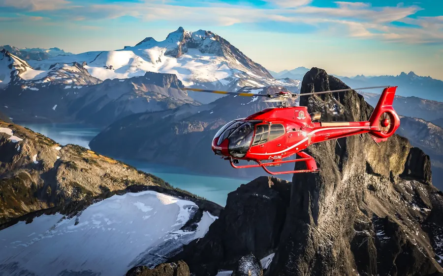 A red helicopter in flight beside dark rock spires at sunrise