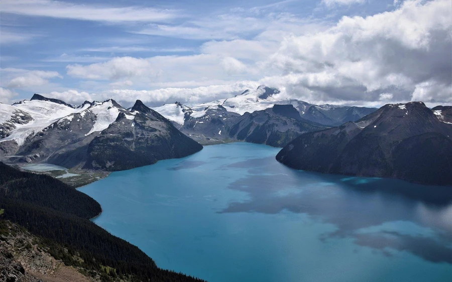 A long turquoise lake below snow-covered peaks and a wide glacier field