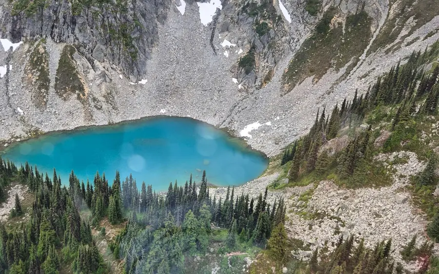 A turquoise alpine lake in a bowl of scree and fir forest, seen from the air